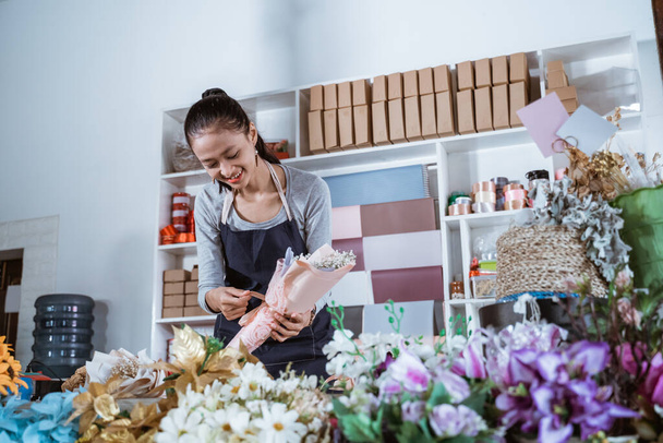 woman working in flower shop wearing apron preparing order - Foto, imagen