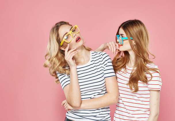 two cheerful girlfriends in striped t-shirts are standing side by side on a pink background lifestyle communication - Photo, Image