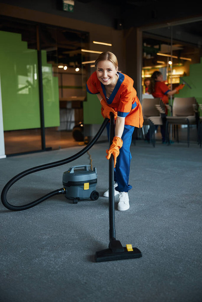 Χαμογελώντας όμορφη καθαρίστρια σκουπίζει το πάτωμα - Φωτογραφία, εικόνα