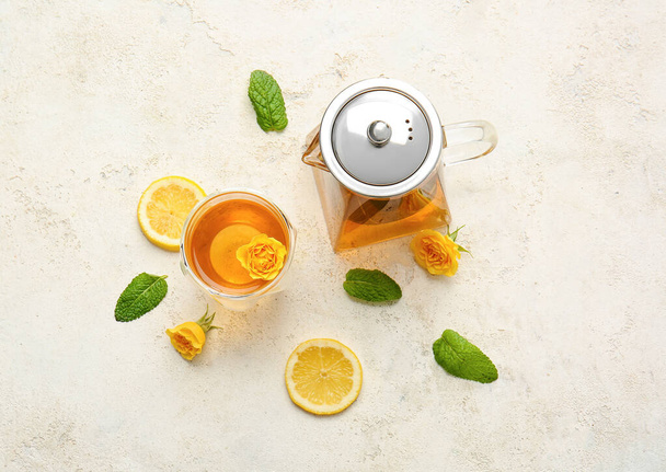 Чайник з гарячим чаєм, склянкою, лимонними та трояндовими квітами на світлому фоні
 - Фото, зображення