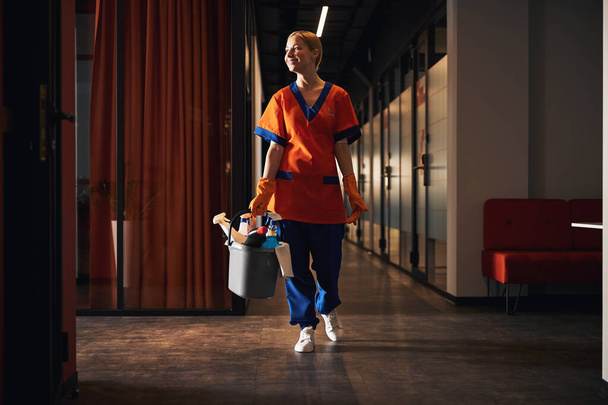 Aangename jonge schoonmaakster loopt langs de kantoorgang - Foto, afbeelding