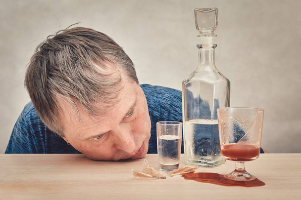 The drunk man put his head on the table in front of a bottle of alcohol. - Fotografie, Obrázek