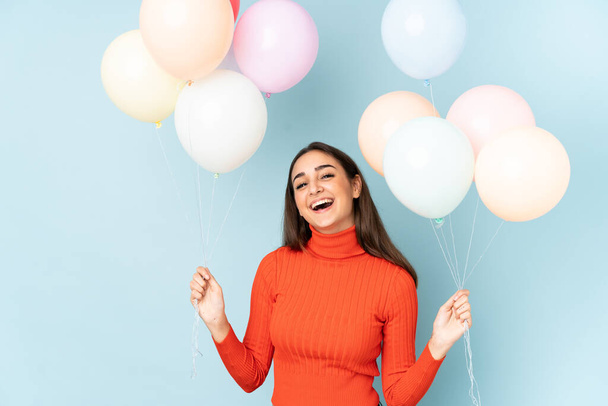 Young woman catching many balloons isolated on blue background - Photo, Image