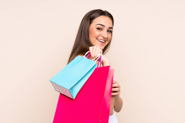 Young caucasian woman isolated on beige background holding shopping bags and looking back - Fotografie, Obrázek