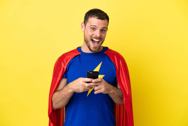Super eroe brasiliano isolato su sfondo giallo sorpreso e l'invio di un messaggio - Foto, immagini