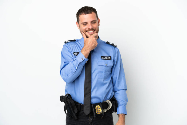 Junger brasilianischer Polizist isoliert auf weißem Hintergrund, zur Seite schauend und lächelnd - Foto, Bild