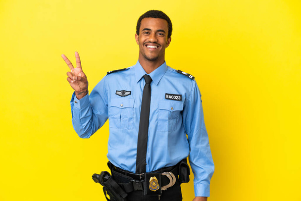 Afroamerikanischer Polizist auf gelbem Hintergrund lächelt und zeigt Siegeszeichen - Foto, Bild