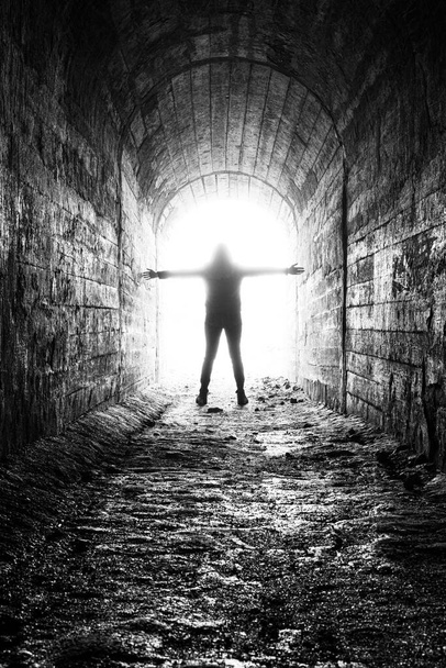 la mujer se sumerge en la luz lechosa al final del túnel. el moribundo sale a la luz al final del pasillo. foto en blanco y negro con efecto de grano - Foto, Imagen