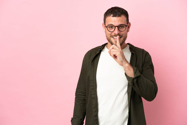Young Brazilian man isolated on pink background showing a sign of silence gesture putting finger in mouth - Foto, imagen