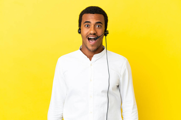 African American Telemarketer man working with a headset over isolated yellow background with surprise facial expression - Valokuva, kuva