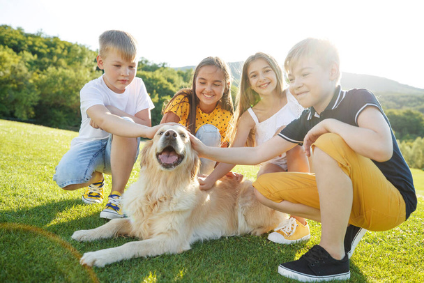 Group of happy children playing on green grass in a spring park with a dog. - Foto, imagen