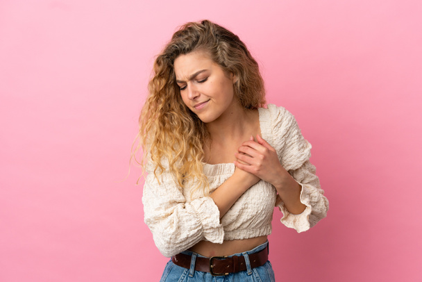 Young blonde woman isolated on pink background having a pain in the heart - Фото, зображення