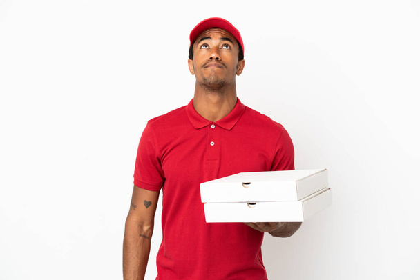 Afroamerikanischer Pizzabote nimmt Pizzakartons über isolierte weiße Wand und schaut auf - Foto, Bild