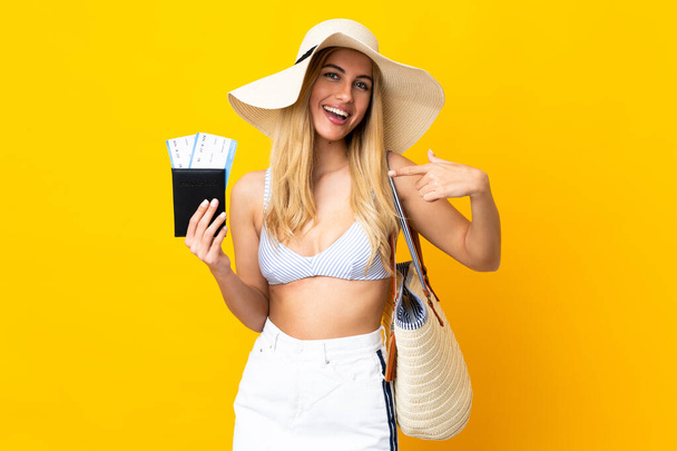 Young Uruguayan blonde woman in swimsuit holding a passport over isolated yellow background and pointing it - Photo, Image