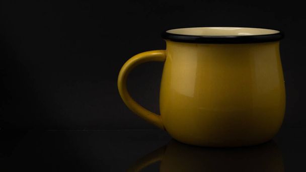 A studio side shot of a yellow mug isolated on a black background - Zdjęcie, obraz