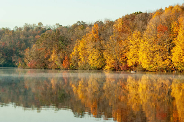 A calm lake surrounded by beautifuautumn foliage during daylight - Zdjęcie, obraz