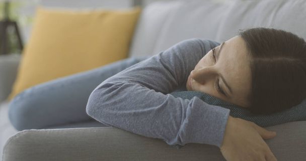 Depressed young woman lying down on the couch at home, stress and mental health concept - Φωτογραφία, εικόνα
