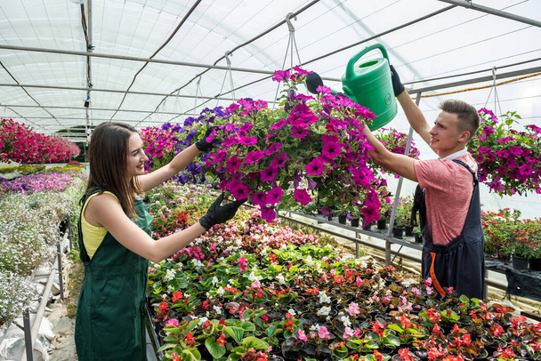 Νεαρό ευτυχισμένο ζευγάρι που δουλεύει με λουλούδια στο βιομηχανικό θερμοκήπιο. Τρόπος ζωής - Φωτογραφία, εικόνα