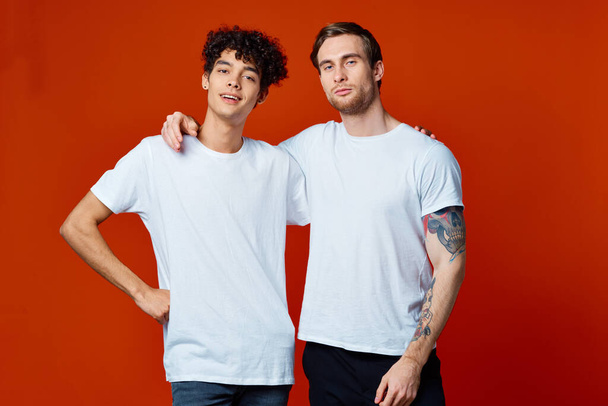 dos amigos en camisetas blancas abraza la comunicación fondo rojo - Foto, imagen