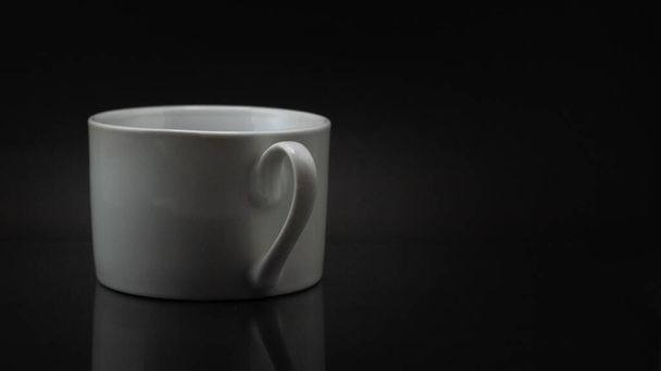 A close up of a white coffee cup isolated on a black background - Фото, изображение