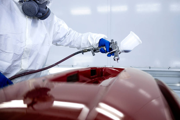Auto schilder in beschermende kleding en masker schilderen auto bumper met metalen verf en vernis in kamer workshop. - Foto, afbeelding