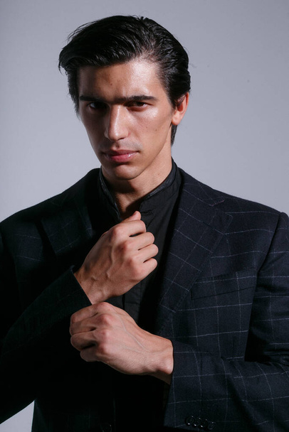 Frontaal portret van brunette man in zwart pak, gearrangeerd zijn knopen op jas, poseert met attitudine in de studio, geïsoleerd op witte achtergrond. Verticaal overzicht. - Foto, afbeelding