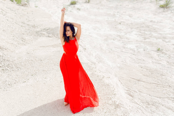 Young woman with hands up wearing the bright red dress. Horizontal outdoors shot. - Фото, изображение