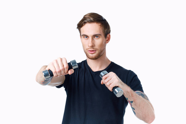 athlete with dumbbells in his hands on a white background in a black t-shirt - Photo, Image