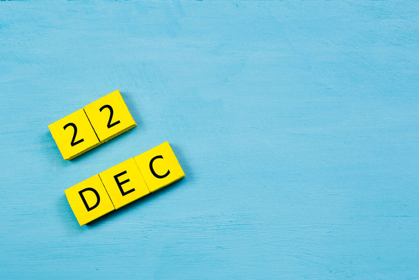 Kalendarz żółtych kostek na niebieskiej drewnianej powierzchni z 22 GRUDZIEŃ i przestrzeń do kopiowania - Zdjęcie, obraz