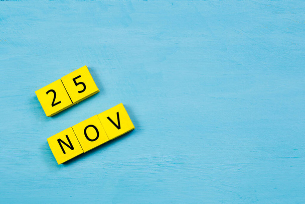 Yellow cubes calendar on blue wooden surface with 25 NOVEMBER and copy space - Photo, Image