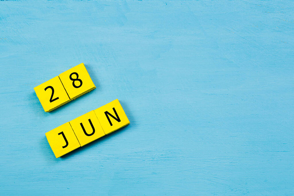 Yellow cubes calendar on blue wooden surface with 28 JUNE and copy space - Photo, Image
