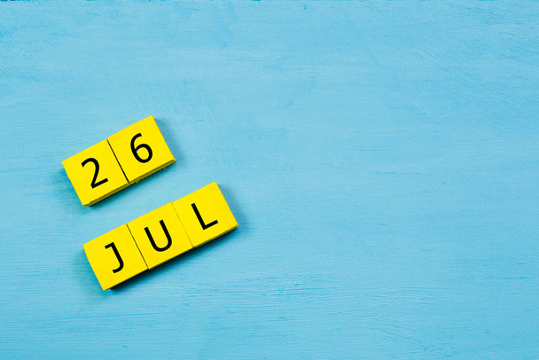 Yellow cubes calendar on blue wooden surface with 26 JULY and copy space - Photo, Image