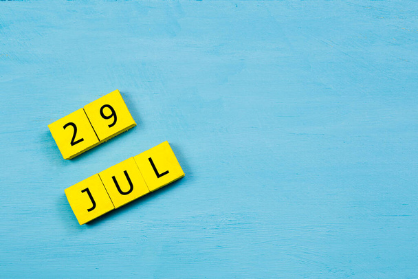 Yellow cubes calendar on blue wooden surface with 29 JULY and copy space - Photo, Image