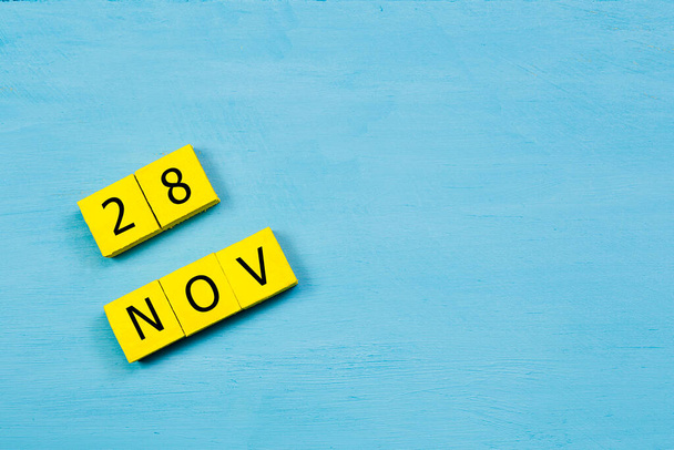 Yellow cubes calendar on blue wooden surface with 28 NOVEMBER and copy space - Photo, Image