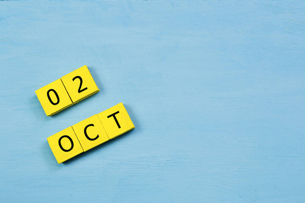 Yellow cubes calendar on blue wooden surface with 02 OCTOBER and copy space - Photo, Image