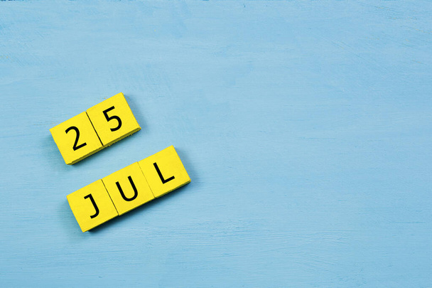 Yellow cubes calendar on blue wooden surface with 25 JULY and copy space - Photo, Image