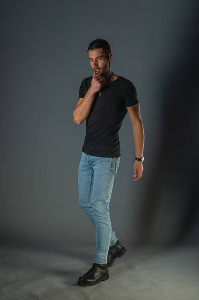 Studio photoshoot of a good-looking man posing in jeans and black shirt - Фото, изображение