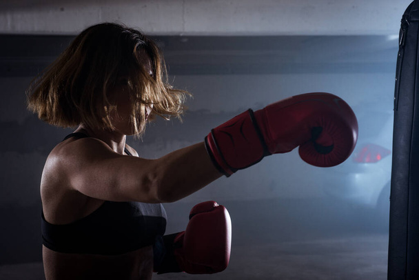 Sportliches Mädchen mit einer kämpferischen Einstellung bei Boxübungen und einem Volltreffer auf rauchigem Hintergrund - Foto, Bild