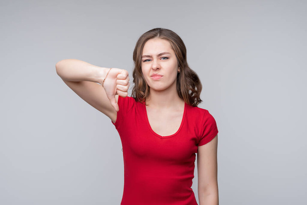 Portrait of displeased young woman showing thumb down gesture on gray background. Human emotions and feelings, facial expression concept - Photo, Image