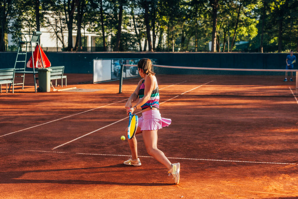 View from the back of a young female paying tennis on a court outside - Photo, Image