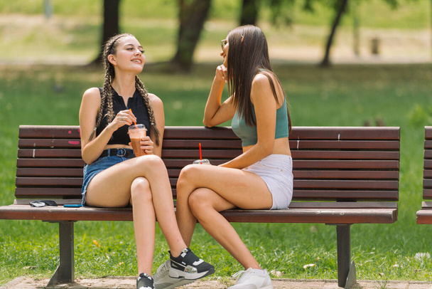 Atrakcyjne dwie kobiety siedzące na ławce w parku w letni dzień - Zdjęcie, obraz