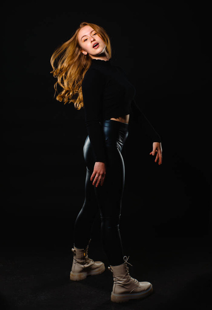Молодая женщина в кожаных черных брюках изолированы на темном фоне - Фото, изображение