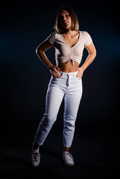Portrait of an attractive trendy girl in beige top posing over black wall - Zdjęcie, obraz
