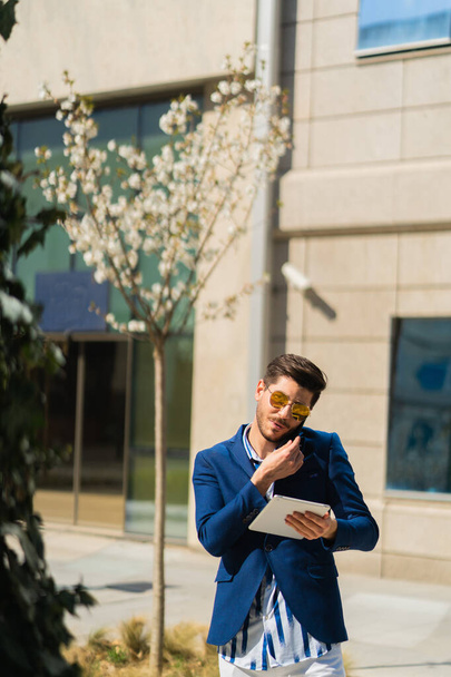 Городской бизнесмен разговаривает по телефону во время работы над планшетом о планах своей компании - Фото, изображение