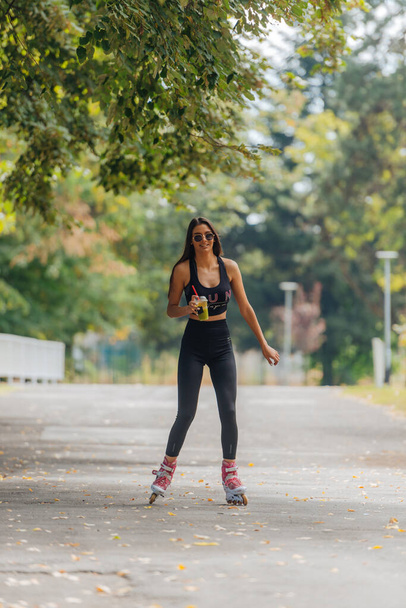 Femme athlétique chaude en roller de vêtements de sport au parc par temps ensoleillé. - Photo, image