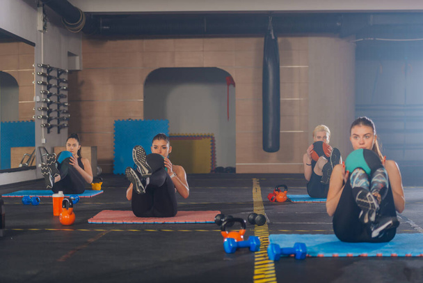 Meninas esportivas atraentes praticando exercícios abdominais com bola de med em um treino de fitness em grupo - Foto, Imagem