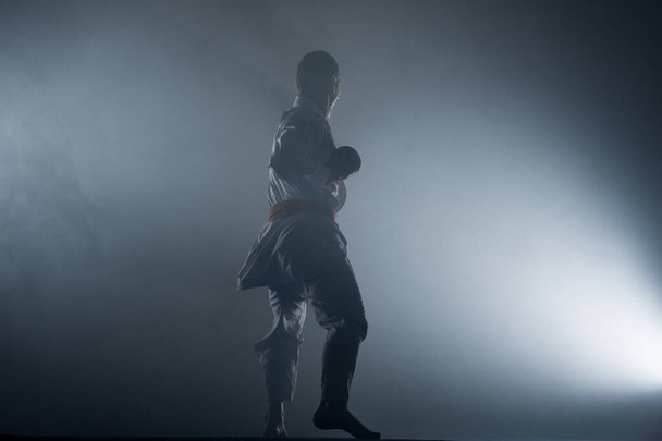Young sporty man in white kimono training karate kata moves in gym - Valokuva, kuva
