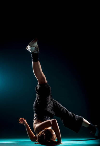 Dance moves performed by an acrobatic flexible female dancer dancing in dark studio - 写真・画像