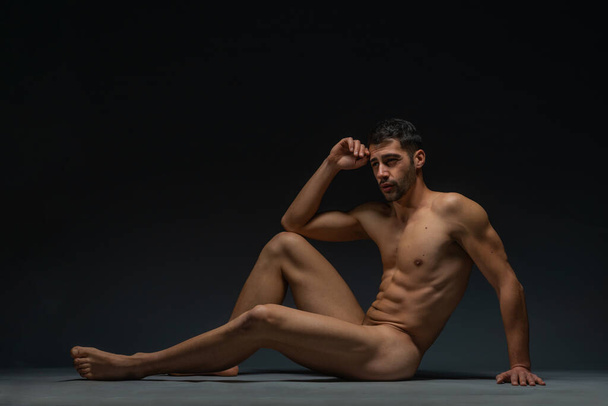 Fashion nude photo of a male model with seductive figure sitting isolated on the floor in a studio - Photo, Image