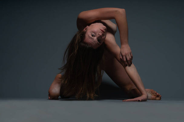 Kopfüber akrobatisches Foto einer jungen nackten Frau, die sich in einem dunklen Studio auf den Boden legt - Foto, Bild